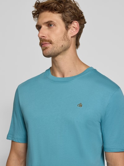 Männermodel trägt Regular Fit T-Shirt aus reiner Baumwolle von Scotch & Soda in Blau mit Logo-Stitching und Rundhalsausschnitt, Nahaufnahme Oberkörper. Rückenlänge bei Größe M: 61 cm.