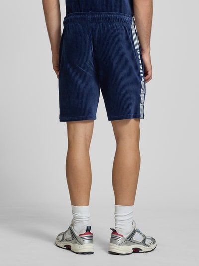 Męski model nosi Shorts aus Cord Modell 'TOMATRO' von Ellesse, granatowy sztruks, elastyczny pas, krój regular fit, widok całej sylwetki od tyłu