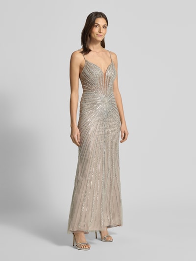 Frauenmodel trägt Slim Fit Abendkleid mit Allover-Ziersteinbesatz von Hey Kyla, semitransparent, mit Spaghettiträgern, Nahtreißverschluss, blickdichtem Unterrock, silberner Glanz auf beige, Ganzkörperansicht von vorne.