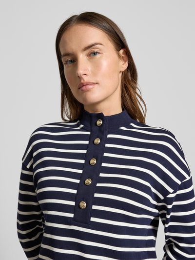 Frauenmodel trägt Ringel Polo Shirt mit Schmuckknopf von Christian Berg Woman in Dunkelblau mit weißen Streifen, gerippter Stehkragen, Nahaufnahme Oberkörper.