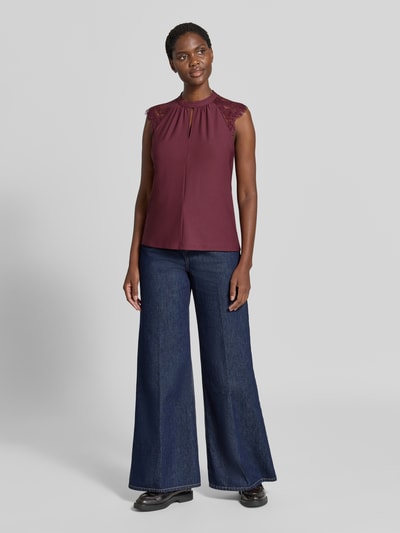 Frauenmodel trägt Regular Fit Kurzarmbluse mit semitransparenter Besatz Modell 'MILLA' von VERO MODA in Dunkelrot, kombiniert mit dunkelblauer Jeans, fließender Stoff, Ganzkörperansicht von vorne. Damen Kurzarmbluse von VERO MODA.