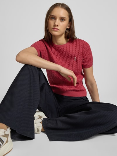 Frauenmodel trägt Kurzarmpullover mit Zopfmuster und Rundhalsausschnitt von Review, reine Baumwolle, Slim-Fit, Logo, Rippbündchen, Ganzkörperansicht von vorne.