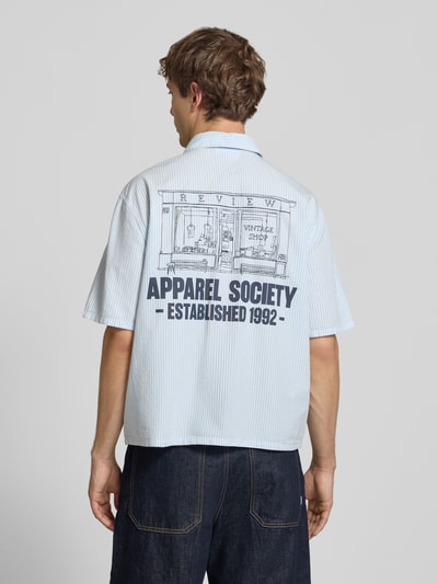 Männermodel trägt Regular Fit Freizeithemd mit 1/2-Arm von REVIEW in Hellblau mit feinen Streifen, Rückseite bedruckt, Ganzkörperansicht Rückansicht. Kontext: Reine Baumwolle, Kentkragen, Knopfleiste, Label-Detail, Rückenlänge 67 cm bei Größe M, Schulterbreite 50 cm, Ärmellänge 28 cm.