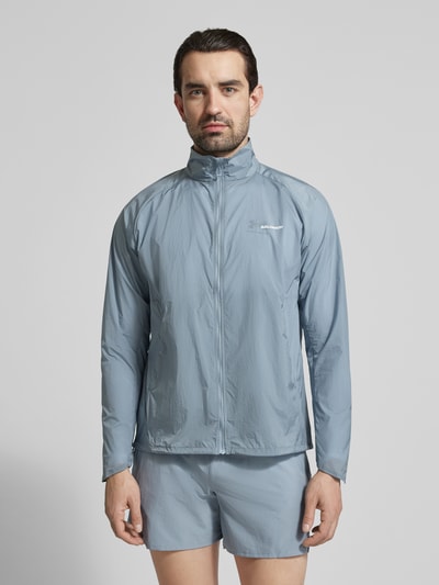 Männermodel trägt Jacke mit Logo und Eingrifftaschen von Salomon in Hellblau, Regular Fit, Stehkragen, Reißverschluss, Ganzkörperansicht von vorne. Rückenlänge 70 cm, Schulterbreite 43 cm, Brustweite 35 cm, Ärmellänge 67 cm.