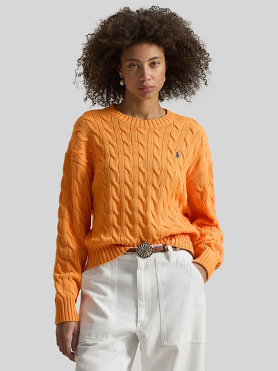 Vrouwenmodel draagt Regular Fit Strickpullover aus reiner Baumwolle van Polo Ralph Lauren in effen oranje met kabelpatroon, logo-stitching, crew neck, lange mouw, geribde boorden, gebreid katoenmateriaal. Nahaufnahme bovenlichaam.