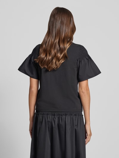 Frauenmodel trägt Regular Fit T-Shirt mit Smok-Detail von Comma aus reiner Baumwolle, ausgestellte Ärmel, kurzärmelig, Rundhalsausschnitt, Rückansicht, Ganzkörperansicht.