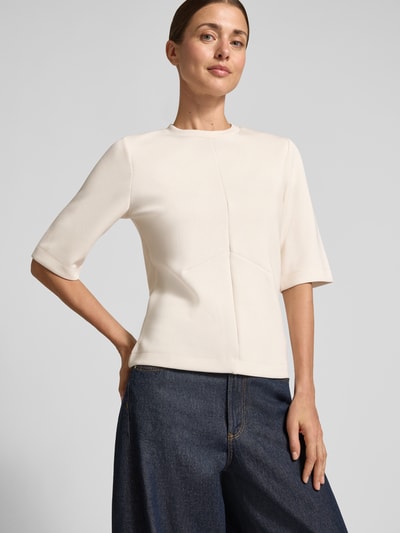 Modelka nosi Regular Fit Sweatshirt mit Ziernähten od Christian Berg Woman, kremowy kolor, gładka tekstura, półrękaw, okrągły dekolt, elastyczny materiał z domieszką modalu, widoczne ozdobne szwy, kontekst: damska bluza, krój regular fit, widok całej sylwetki z przodu.
