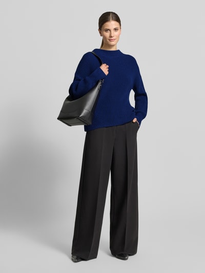 Frauenmodel trägt Strickpullover mit Stehkragen Modell 'TELLINA' von Someday, Baumwoll-Mix in Blau, strukturierte Oberfläche, lockerer Schnitt, gerippte Abschlüsse, kombiniert mit weiter schwarzer Hose, Ganzkörperansicht von vorne.