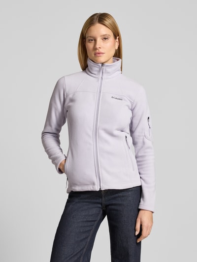 Frauenmodel trägt Slim Fit Fleecejacke mit Ärmeltasche Modell 'Fast Trek™ II' von Columbia in hellem Fliederton, Ganzkörperansicht von vorne. Kontext: Damen Fleecejacke mit Stehkragen, durchgehendem Reißverschluss, Label-Detail, Reißverschlusstaschen, elastischen Abschlüssen, Rückenlänge 63 cm, Schulterbreite 40 cm, Brustweite 45 cm, Ärmellänge 62 cm.