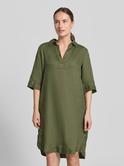 Frauenmodel trägt knielanges Leinenkleid Modell 'DERRY' von 0039 Italy in Oliv, gerader Schnitt, Hemdblusenkragen, V-Ausschnitt, Ganzkörperansicht von vorne.