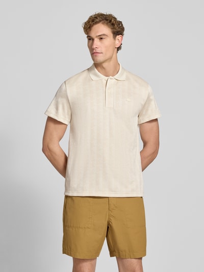 Männermodel trägt Classic Fit Poloshirt mit Logo-Detail von Lacoste in Beige, kombiniert mit hellbraunen Shorts, Ganzkörperansicht von vorne. Herren Poloshirt von Lacoste.