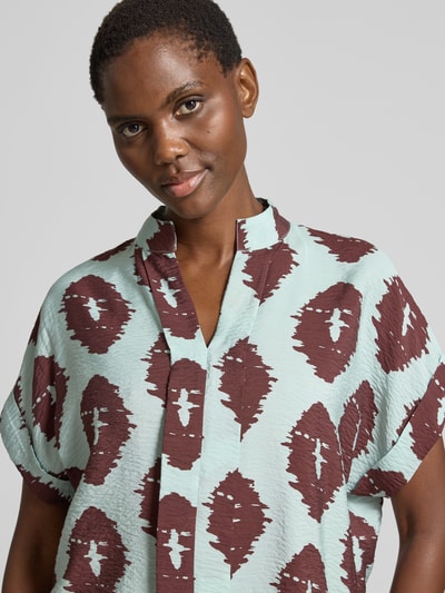 Vrouwenmodel draagt Bluse aus Viskose-Mix mit Ärmelaufschlag van Christian Berg Woman in turquoise en bruin met tuniekkraag, straight fit en mouwomslag, ruglengte bij maat 36: 69 cm, nahaufnahme bovenlichaam.