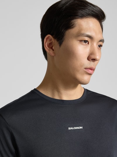 Männermodel trägt Funktionsshirt mit Logo und Rundhalsausschnitt von Salomon, Regular Fit, schwarze Struktur, Nahaufnahme Oberkörper.