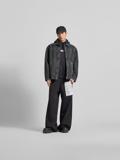 Männermodel trägt Loose Fit Stoffhose mit Logo-Print von MM6 Maison Margiela in Schwarz, reine Baumwolle, Ganzkörperansicht von vorne.