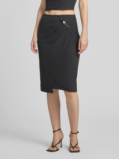 Frauenmodel trägt Slim Fit Rock in Knielänge Modell 'Karole' von GUESS, Elastischer-Material-Mix, Schwarz, Dornschließe, Nahaufnahme Unterkörper, Ganzkörperansicht von vorne. Bundweite 36 cm, Gesamtlänge 65 cm, Größe S.