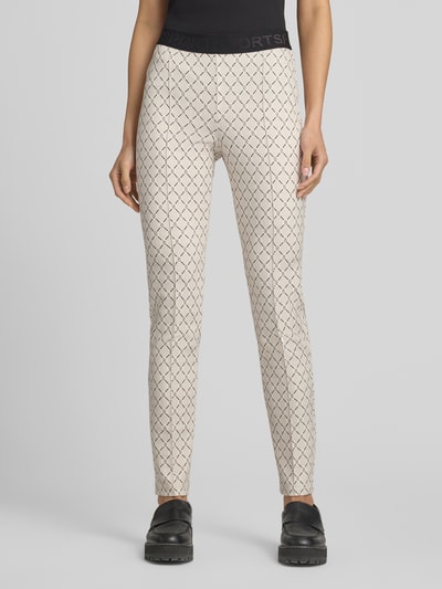 Frauenmodel trägt Slim Fit Hose mit Logo-Muster von Marc Cain, Material-Mix mit Stretch-Anteil, Regular Waist, Längsnähte, elastischer Bund, Farbe Beige mit schwarzem Logo-Muster, Ganzkörperansicht von vorne.