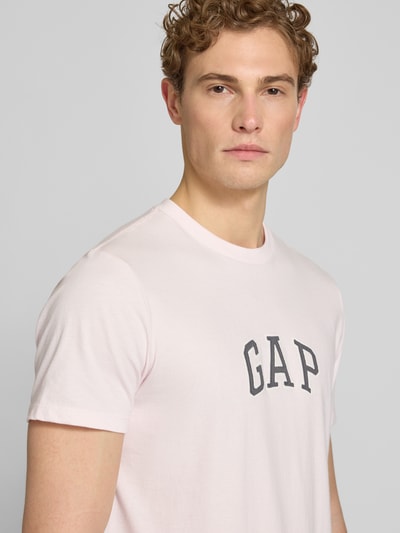 Männermodel trägt T-Shirt mit Logo-Patch und Rundhalsausschnitt von GAP in zartem Rosa aus reiner Baumwolle, Straight Fit, Nahaufnahme Oberkörper. Rückenlänge bei Größe M: 70 cm.