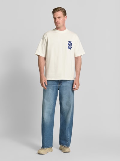 Męski model nosi T-Shirt mit rückseitigem Motiv-Print von Jake*s Studio Men z bawełny w kroju regular fit, kremowy kolor, haft, okrągły dekolt, długość tyłu w rozmiarze M: 68 cm, Ganzkörperansicht von vorne.