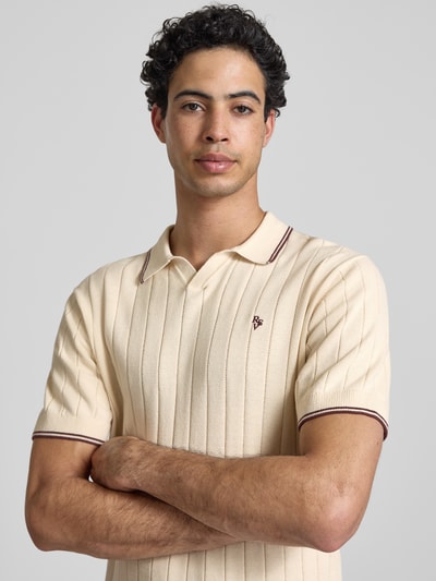 Męski model nosi Slim Fit Polo-Strickshirt mit Logo-Stickerei od REVIEW, czysta bawełna, krój slim fit, prążkowana faktura, kremowy, detal haftu, długość tyłu w rozmiarze M: 65 cm, zbliżenie górnej części ciała