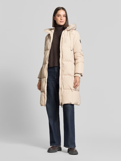 Frauenmodel trägt Regular Fit Mantel in Stepp-Optik Modell 'Nova' von MOS MOSH, beige, Zweiwege-Reißverschluss, Eingrifftaschen, Ganzkörperansicht von vorne.