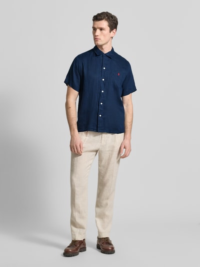Męski model nosi Regular Fit Freizeithemd aus reinem Leinen von Polo Ralph Lauren, granatowa koszula z krótkim rękawem, jednolita faktura, guzikami i logo, lekka lniana tkanina, widok całej sylwetki z przodu.