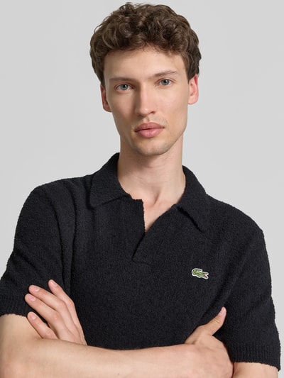 Männermodel trägt Regular Fit Poloshirt aus Baumwoll-Mix von Lacoste, unifarben schwarz, Bouclé-Struktur, Label Patch, Nahaufnahme Oberkörper.