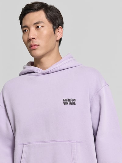 Mężczyznamodel nosi Hoodie mit Logo Modell 'PLIZZY' von American Vintage z bawełny, krój relaxed fit, kieszeń kangurka, logo, jasnofioletowy kolor, długość rękawów 60 cm, długość tyłu 66 cm, zbliżenie na górną część ciała