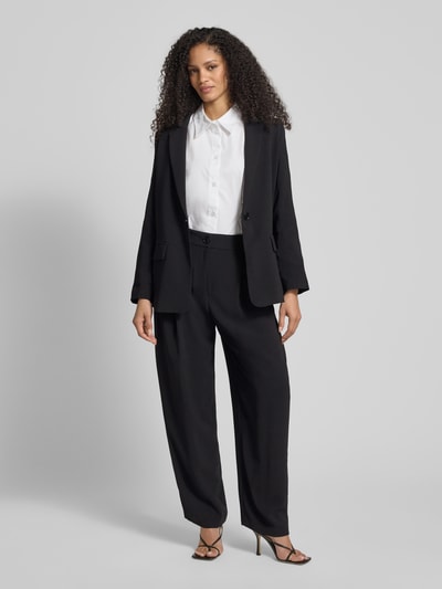 Frauenmodel trägt Relaxed Fit Hose mit Bundfalten von ARMANI EXCHANGE in Schwarz, kombiniert mit weißer Bluse, Ganzkörperansicht von vorne. Bundfalten, Eingrifftaschen, Knopf- und Reißverschluss, Bundweite 38 cm, Innenbeinlänge 76 cm bei Größe 36.