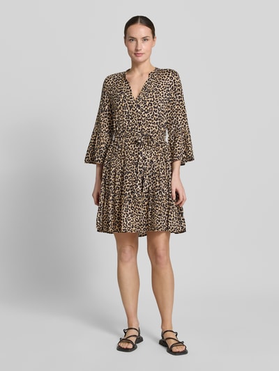 Vrouwenmodel draagt Tailliertes Tunikakleid aus reiner Viskose Modell 'MELBA' van Vero Moda met all-over patroon, getailleerde fit, mini lengte, V-hals, trompetmouwen, volantzoom, ceintuurlussen en bindriem van pure viscose, frontale volledige lichaamsweergave.