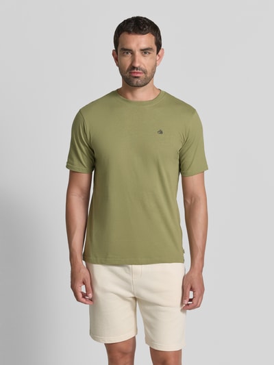 Männermodel trägt T-Shirt mit Label-Stitching und Rundhalsausschnitt von Scotch & Soda in Olive, reine Baumwolle, Regular Fit, Ganzkörperansicht von vorne.