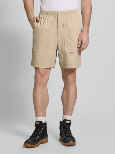 Männermodel trägt Regular Fit Shorts mit Logo-Patch Modell 'Landroamer' von COLUMBIA in Beige, elastischer Bund, aufgesetzte Taschen, Nahaufnahme Oberschenkelansicht.