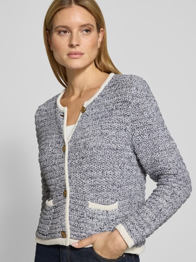 Modelka kobieca nosi Strickjacke mit Rundhalsausschnitt und Knopfleiste od Christian Berg Woman Selection, czarno-biała melanżowa tekstura, krój regular fit, czysta bawełna, długość tyłu w rozmiarze 36: 54 cm, długość rękawa w rozmiarze 36: 66 cm, półzbliżenie na górną część ciała z przodu.
