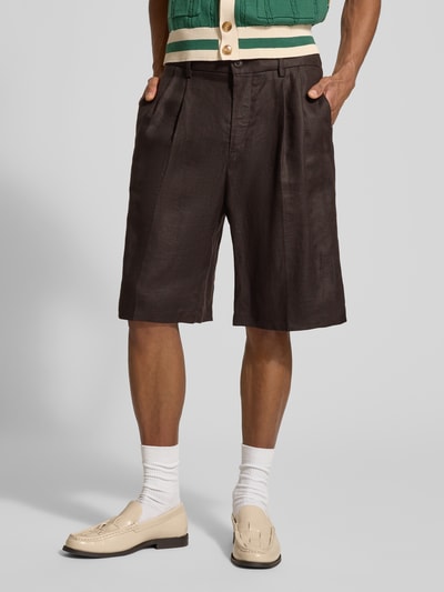 Mężczyzna nosi Leinenshorts aus reinen Leinen od Drykorn, z czystego lnu, luźny krój, kieszenie, fałdy, kolor ciemny brąz, widok z przodu na całe ciało. Szerokość w rozmiarze 33: 44 cm, długość nogawki wewnętrznej: 25 cm.
