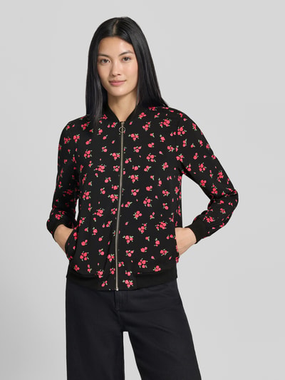 Frauenmodel trägt Regular Fit Blouson mit Allover-Muster Modell 'COCO' von VERO MODA, schwarz mit roten Blumen, Nahaufnahme Oberkörper. Damen Bomberjacke / Blouson.