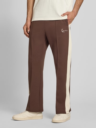 Männermodel trägt Straight Fit Sweatpants mit Logo-Stitching von KARL KANI in Braun mit cremefarbenen Seiteneinsätzen, Elastischer-Material-Mix, Ziernähte und Elastischer Bund, Herren Sweatpants, Ganzkörperansicht von vorne.