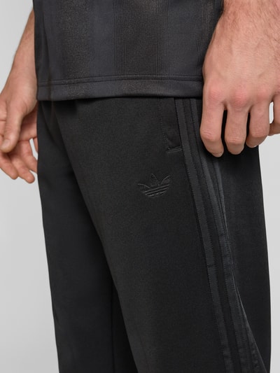 Männermodel trägt Straight Fit Sweatpants mit elastischem Bund von adidas Originals in Schwarz, Baumwoll-Mix, Eingrifftaschen, Nahaufnahme Oberschenkel.