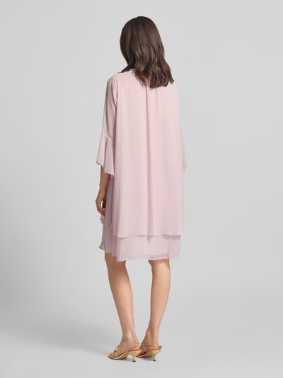 Frauenmodel trägt Knielanges Kleid mit Schleifen-Detail Modell 'Denia' von JOOP! in zartem Rosa, fließender Stoff, Lagenlook, Ganzkörperansicht Rückansicht.