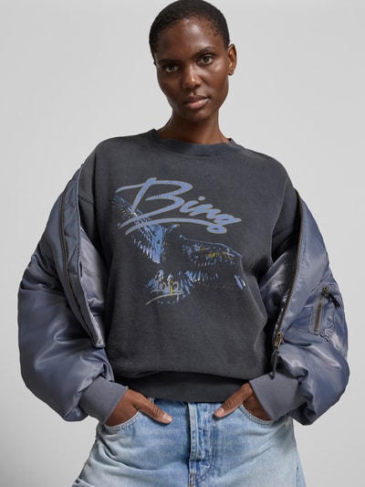 Frauenmodel trägt Regular Fit Sweatshirt mit Motiv-Print von Anine Bing aus reiner Baumwolle, dunkle Farben, Elastische Abschlüsse, Nahaufnahme Oberkörper.