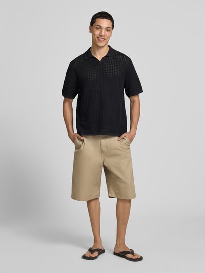 Męski model nosi Regular Fit Poloshirt mit V-Ausschnitt von Jack & Jones z bawełny, krój regular fit, dzianina, czarny, długość tyłu 67 cm w rozmiarze M, widok całej sylwetki z przodu.