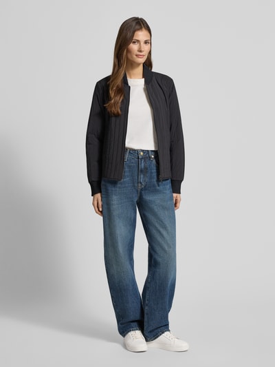 Vrouwenmodel draagt Jacke met Stehkragen und Eingrifftaschen van Scotch & Soda, regular fit, zwart, met labeldetail, ganzlichaamsvooraanzicht. Ruglengte maat S 57 cm, schouderbreedte 44 cm, borstwijdte 50 cm, mouwlengte 63 cm.