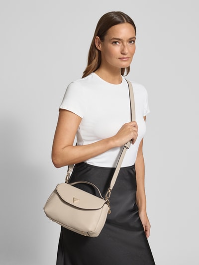 Frauenmodel trägt Shoulder Bag in Leder-Optik Modell 'Evie' von Guess, beige, Logo-Detail, abnehmbarer Schulterriemen, Nahaufnahme Oberkörper.