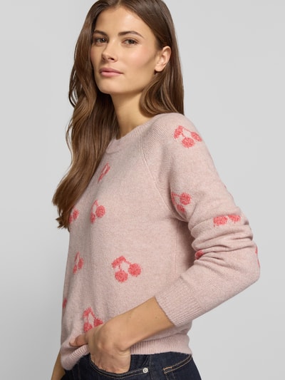 Vrouwenmodel draagt Regular Fit Strickpullover mit Intarsien Modell 'DOFFY INTARSIA' van Vero Moda, roze kleur, all-over patroon, crew neck, lange mouwen, geribde boorden, gebreide textuur. Halfbody aanzicht schuin van voren.