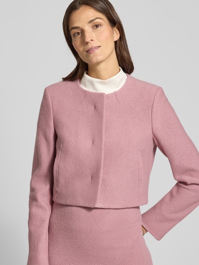 Modelka kobieca nosi Boxy Fit Kurzblazer aus reiner Schurwolle Modell 'JICENA' od BOSS w jednolitym jasnoróżowym kolorze, widok z przodu, zbliżenie na górną część ciała. Tekstura wełny, długi rękaw, ukryte guziki, boczne kieszenie, okrągły dekolt, sportowy detal na rękawie.