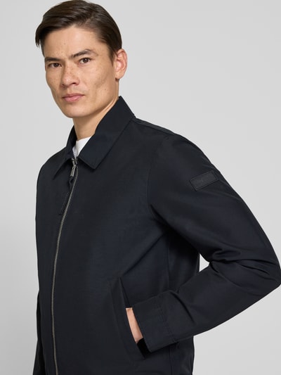 Mannenmodel draagt Regular Fit Blouson met elastische zoom van Marc O'Polo, effen zwart, lange mouwen, rits, label patch, zijzakken, opstaande kraag, close-up bovenlichaam.