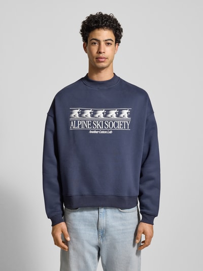 Männermodel trägt Sweatshirt mit Label-Print von ANOTHER COTTON LAB, dunkelblau, Baumwoll-Mix, Lockerer-Schnitt, Gerippte-Abschlüsse, Rundhalsausschnitt, Ganzkörperansicht von vorne.