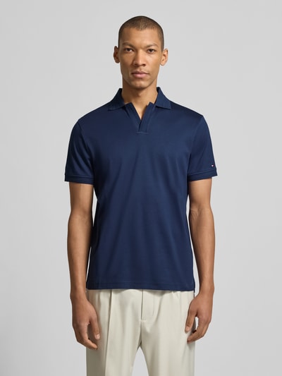 Männermodel trägt Regular Fit Poloshirt aus reiner Baumwolle von Tommy Hilfiger in Dunkelblau, unifarben mit Polokragen und Logo-Detail, Ganzkörperansicht von vorne.