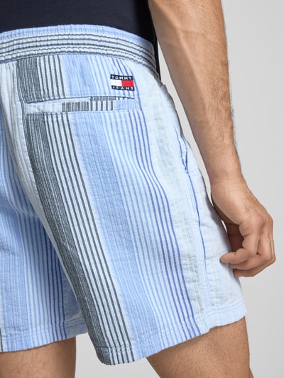 Mężczyzna nosi Relaxed Fit Shorts aus reiner Baumwolle von Tommy Jeans, efekt: wzór na całej powierzchni, krój relaxed fit, naszywka z logo, elastyczny ściągacz z tunelem, wpuszczane kieszenie, wykończenie materiału: dobby, 100% bawełna, detailaufnahme.