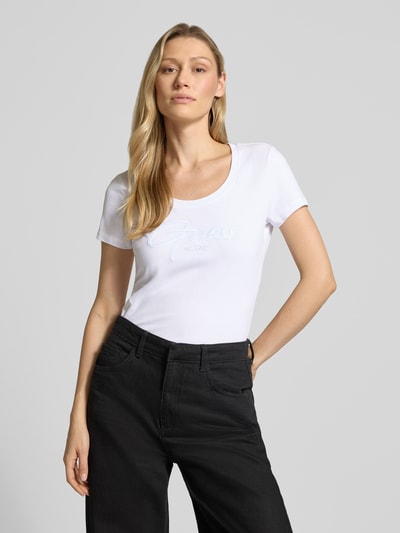 Frauenmodel trägt T-Shirt mit U-Ausschnitt Modell 'SCRIPT' von Guess aus Baumwoll-Elasthan-Mix, körpernaher Schnitt, Label-Stitching, Nahaufnahme Oberkörper.