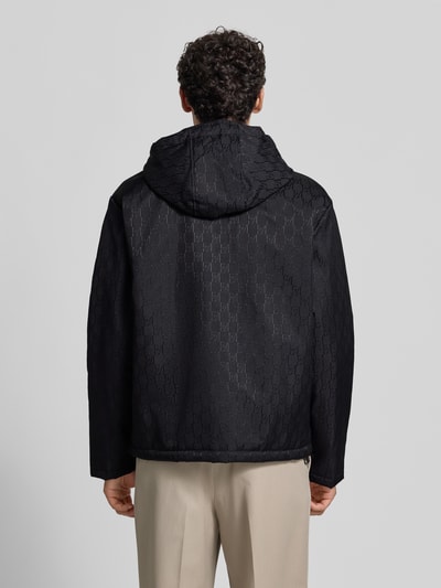Männermodel trägt Regular Fit Jacke mit Allover-Logo-Print von Emporio Armani in Schwarz, leichte Struktur, Ganzkörperansicht Rückansicht. Kontext: Damen Jacke, Logo-Applikation, Kapuze mit Tunnelzug, Zweiwege-Reißverschluss, Eingrifftaschen, Rückenlänge 61 cm, Schulterbreite 47 cm, Brustweite 58 cm, Ärmellänge 65 cm.