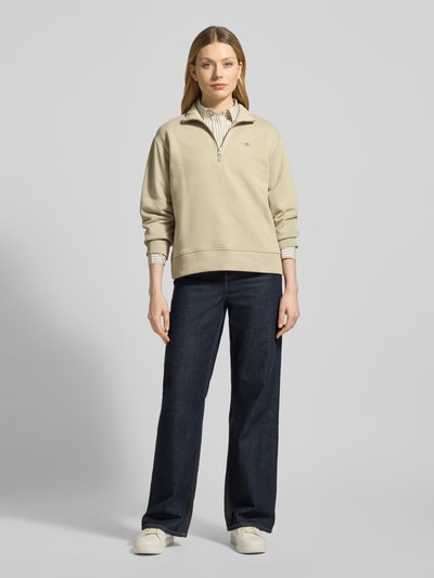 Modelka nosi bluza 'Sweatshirt mit Baumwoll-Anteil' od Gant, mieszanka bawełny, luźny krój, kołnierz zapinany, wyhaftowane logo, prążkowane wykończenia, jasny beż, gładka tekstura, pełen widok z przodu